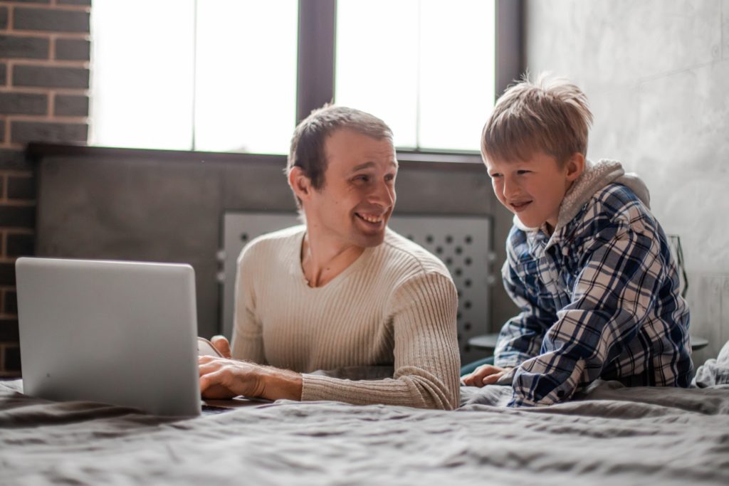 Dad and Son are Sitting in the Bedroom with Laptop
